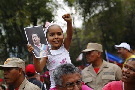 A girl gestures while holding a photo of Venezuela's late president Hugo Chavez during a rally with a Bolivarian militia in Caracas March 15, 2014. REUTERS/Jorge Silva