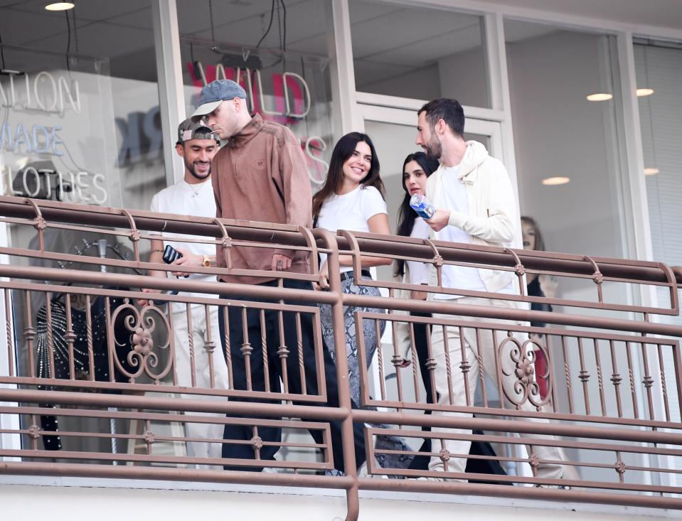 bad bunny and kendall jenner walking on an outdoor patio, laughing and chatting with friends 