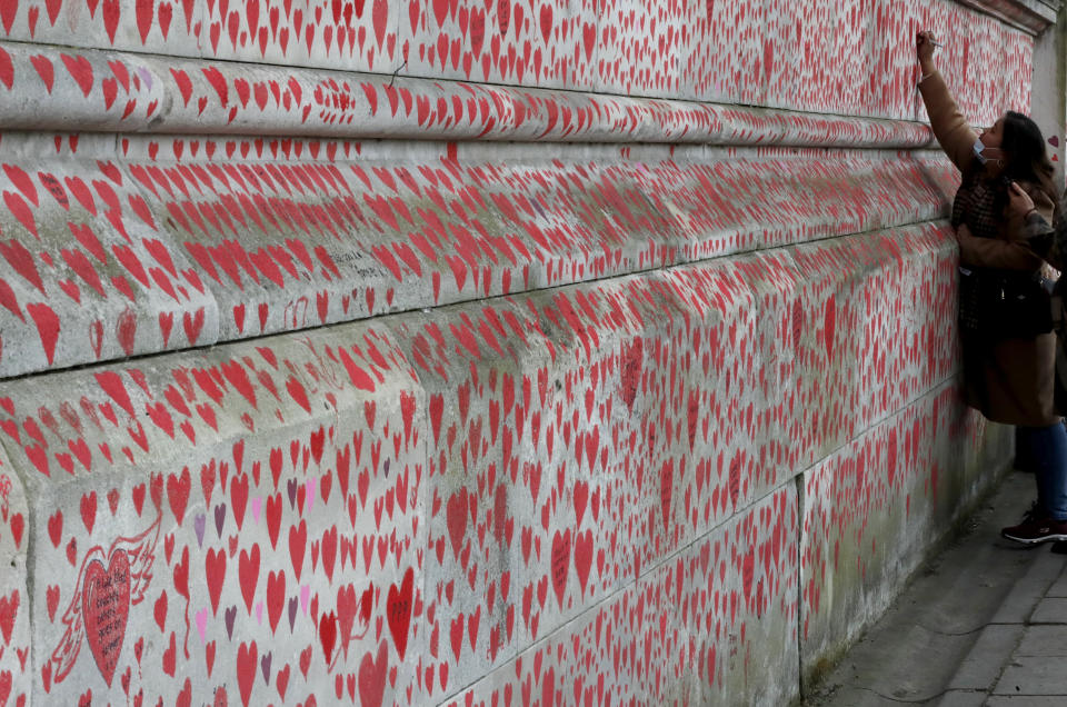 People paint red hearts marking the completion of the approximately 150,000 hearts being painted onto the National Covid Memorial Wall to commemorate all those who have died of coronavirus, on the Thames Embankment opposite the Houses of Parliament in London, Thursday, April 8, 2021. Bereaved families want the wall of painted hearts to remain a site of national commemoration and are asking the Prime Minister to help make the memorial permanent. (AP Photo/Frank Augstein)