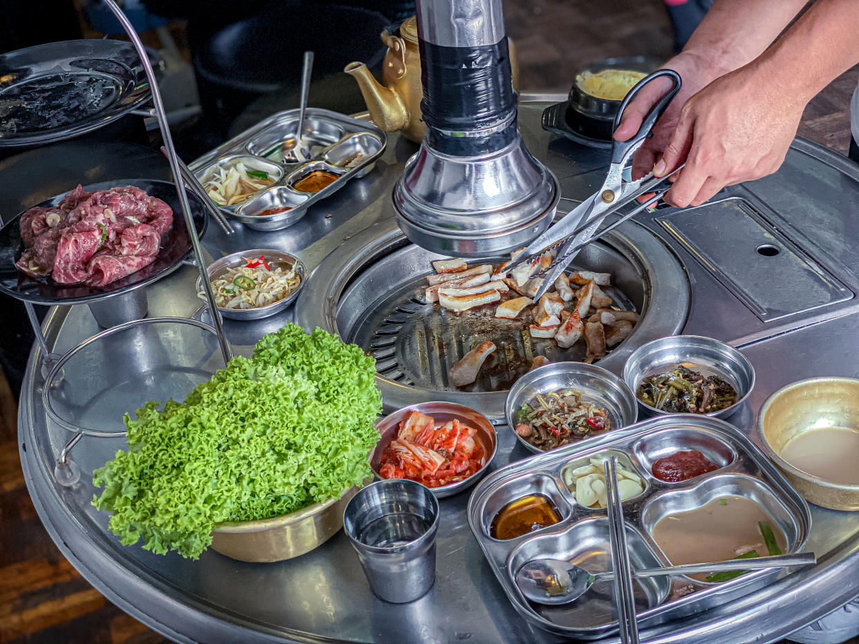 A restaurant server assisting customer with the grilling in a korean BBQ restaurant setup with various side dishes (Banchan)