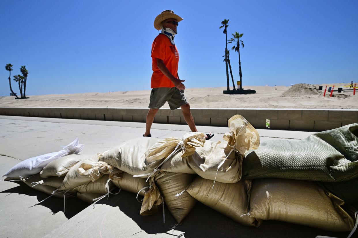 A man walks past sand bags placed to protect beach front homes in Seal Beach, California on August 18, 2023, as they prepare for hurricane Hilary. (AFP via Getty Images)