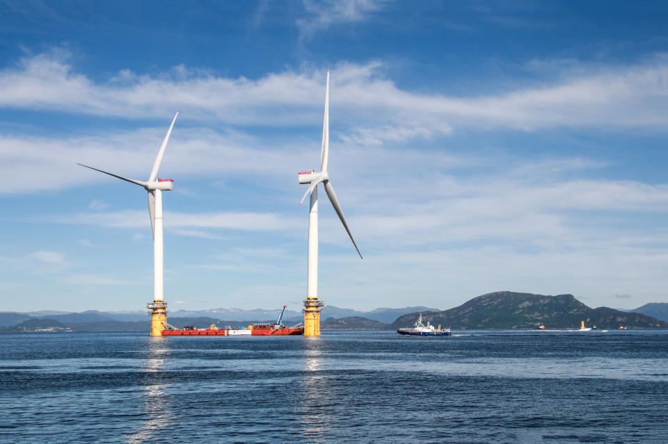 Two wind turbines stand in the ocean. (Source: Getty)