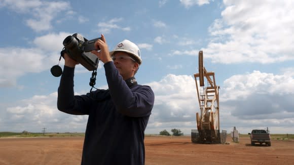 Person holding viewing equipment near an oil pump.