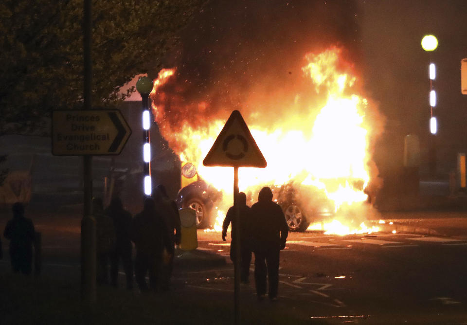 Masked loyalists are seen after hijacking and setting a car on fire at the Cloughfern roundabout in Newtownabbey, Belfast, Northern Ireland, Saturday, April 3, 2021. Masked men threw petrol bombs and hijacked cars in the Loyalist area North of Belfast. Loyalists and unionists are angry about post-Brexit trading arrangements which they claim have created barriers between Northern Ireland and the rest of the UK. (Peter Morrison/PA via AP)