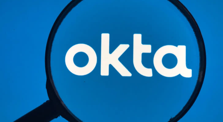 A magnifying glass zooms in on the Okta (OKTA) logo.