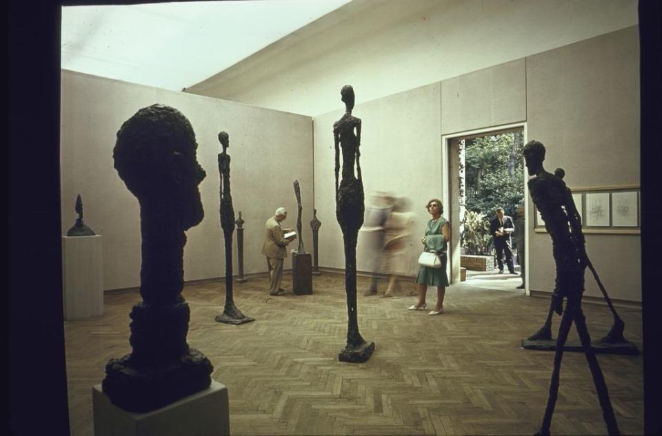 Visitors viewing tall, slender sculptures in an art gallery setting