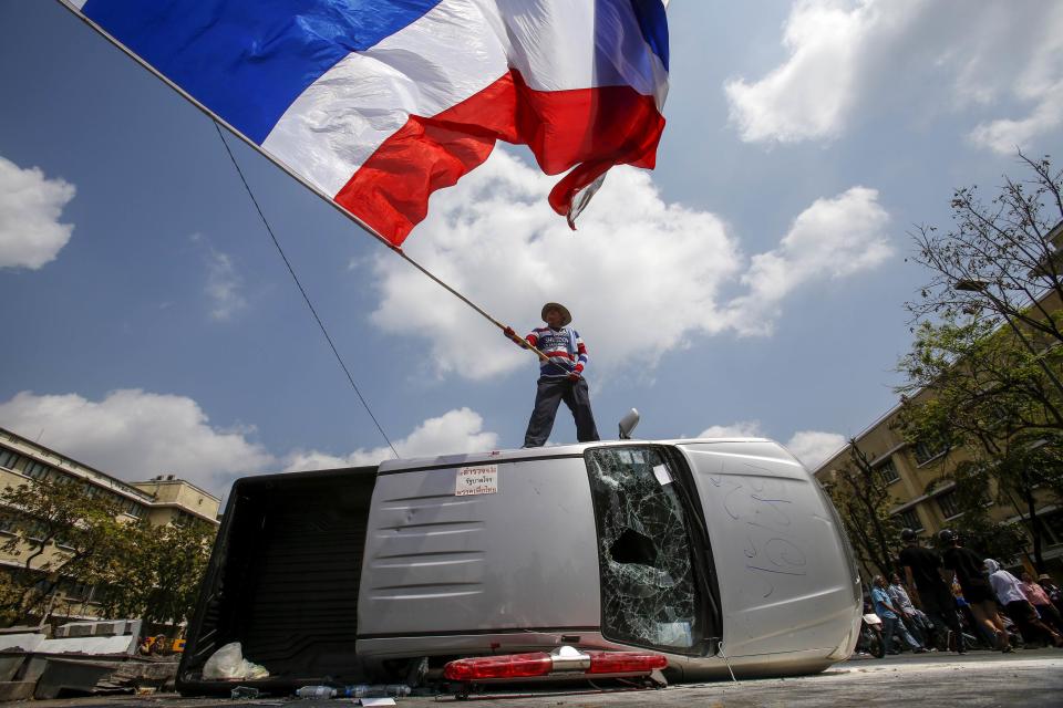 An anti-government protester stands on a damaged police vehicle as he waves a Thai national flag after clashes with riot police officers in Bangkok