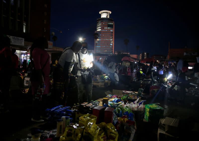 A mam counts money next to a groceries stall at a roadside night market in central Harare