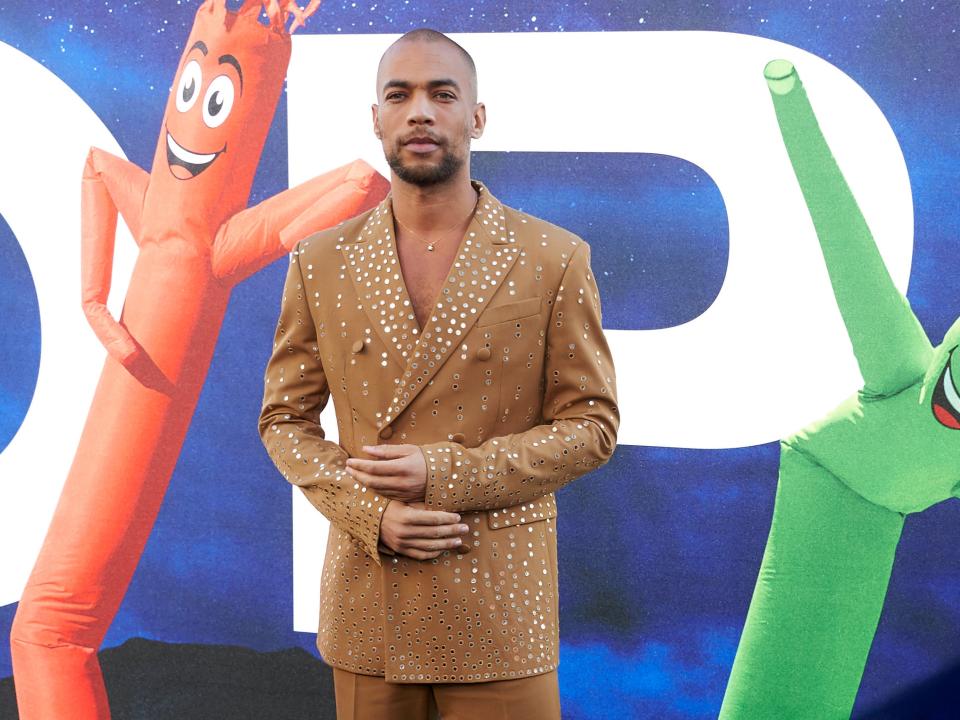 Kendrick Sampson adjusting the cuffs of his golden jacket while posing at the premier of "NOPE"