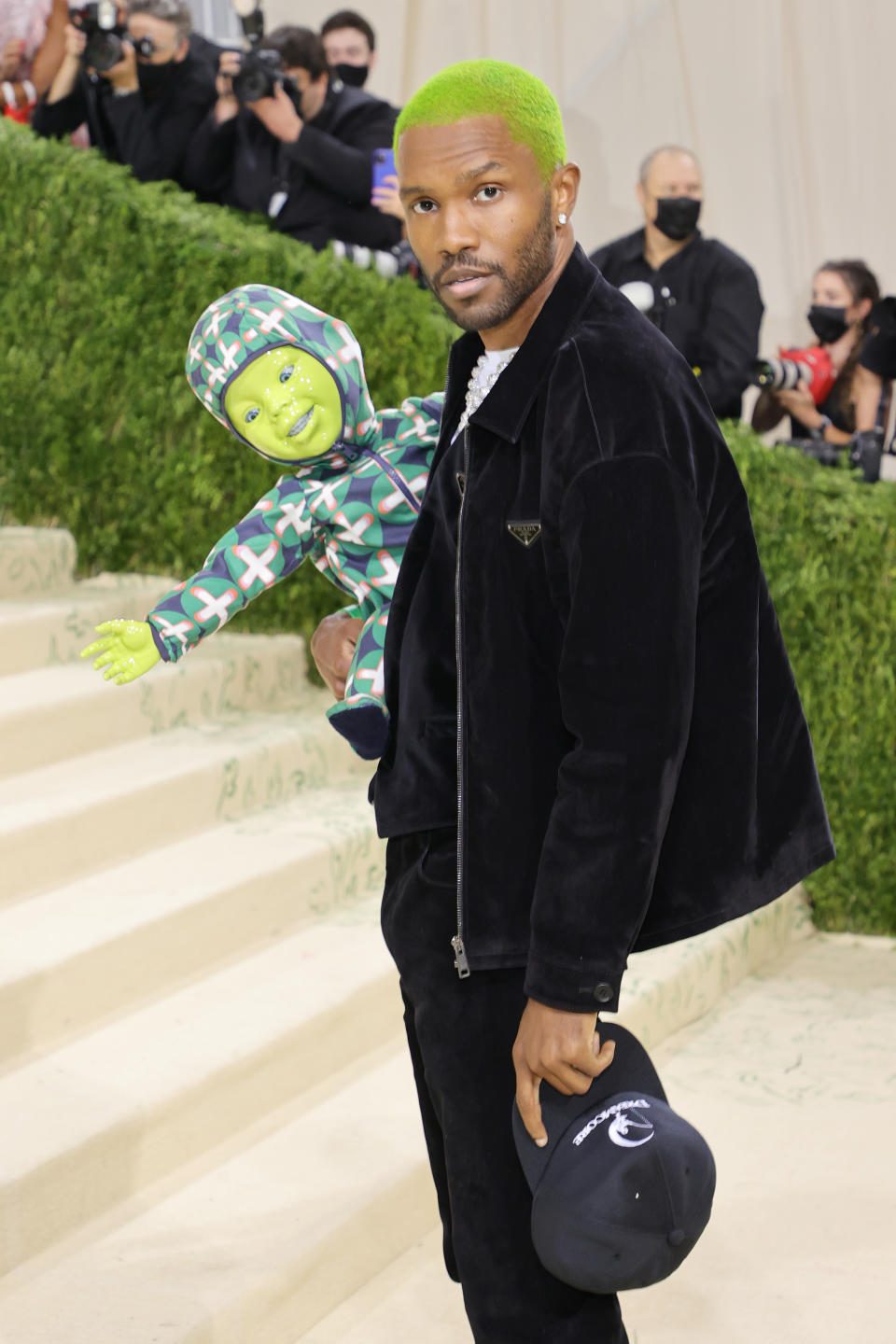 American singer Frank Ocean wearing black with green hair and holding doll at Met Gala.