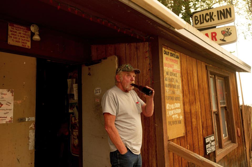 Dave Ferner drinks a beer while watching multiple homes burn in central Doyle, Calif., as the Sugar Fire, part of the Beckwourth Complex Fire, tears through town on Saturday, July 10, 2021. Ferner said he saved his home using a bulldozer earlier in the day. (AP Photo/Noah Berger)