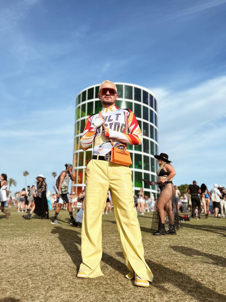 christian standing at coachella in yellow pants and racer shirt