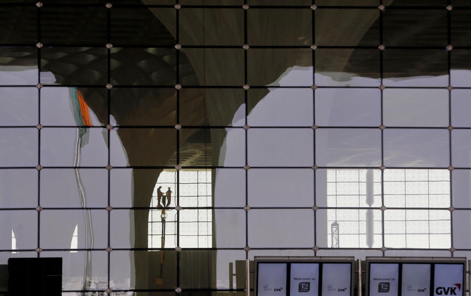 In this Wednesday, Jan. 8, 2014 photo, workers are reflected in a window at the new airport terminal at the Chhatrapati Shivaji International Airport in Mumbai, India. India's overcrowded financial capital unveils its long-awaited $2 billion new airport terminal Friday, an ambitious, art-filled space that developers hope will be a showcase success in a country struggling to modernize inadequate infrastructure that is holding back economic growth. (AP Photo/Rajanish Kakade)