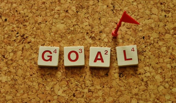 scrabble letters spelling goal on a corkboard, with a small red flag