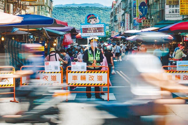 台北市昨日新增54例確診。圖為員警站在市場入口處舉牌，提醒民眾配戴口罩做好防疫。（郭吉銓攝）