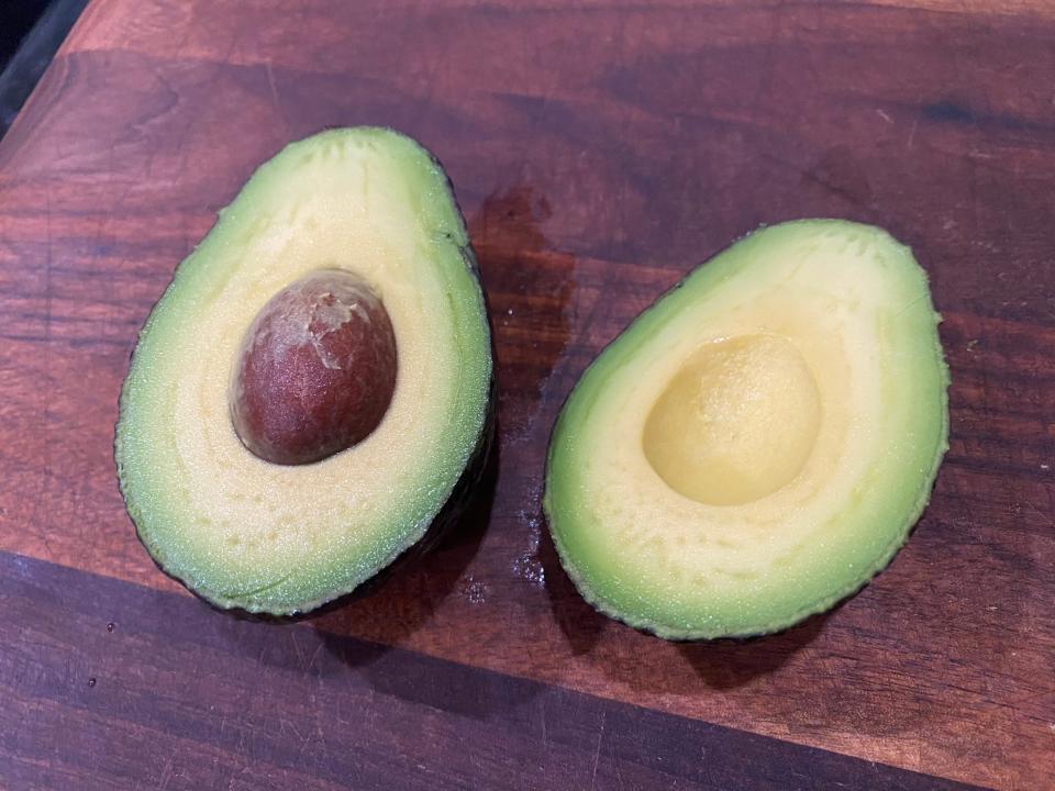A perfect avocado cut in half lays on a cutting board