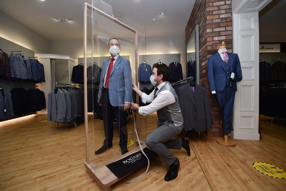 BELFAST, NORTHERN IRELAND - JUNE 12: Tailor Gary Keenan (R) of Bogart Menswear measures up a suit using a customer pod designed to keep customers safe from Covid-19 after their store reopened for business on June 12, 2020 in Belfast, Northern Ireland. After being shuttered for months to curb the spread of Covid-19, retailers here reopened with social distancing measures, a few days ahead of when similar businesses can reopen in England. (Photo by Charles McQuillan/Getty Images)