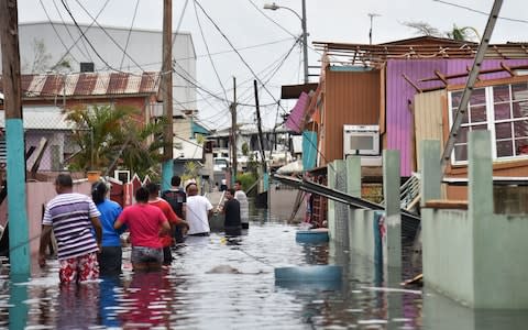 People walk in a flooded street next to damaged houses in Catano town, in Juana Matos, Puerto Rico - Credit: HECTOR RETAMAL/AFP/Getty Images