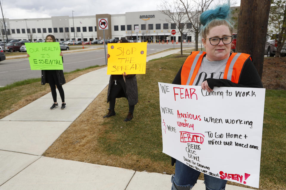 Employee Tonya Ramsay, right, holds a sign outside the Amazon DTW1 fulfillment center in Romulus, Mich., Wednesday, April 1, 2020. Employees and family members are protesting in response to what they say is the company's failure to protect the health of its employees amid the new coronavirus COVID-19 outbreak. (AP Photo/Paul Sancya)