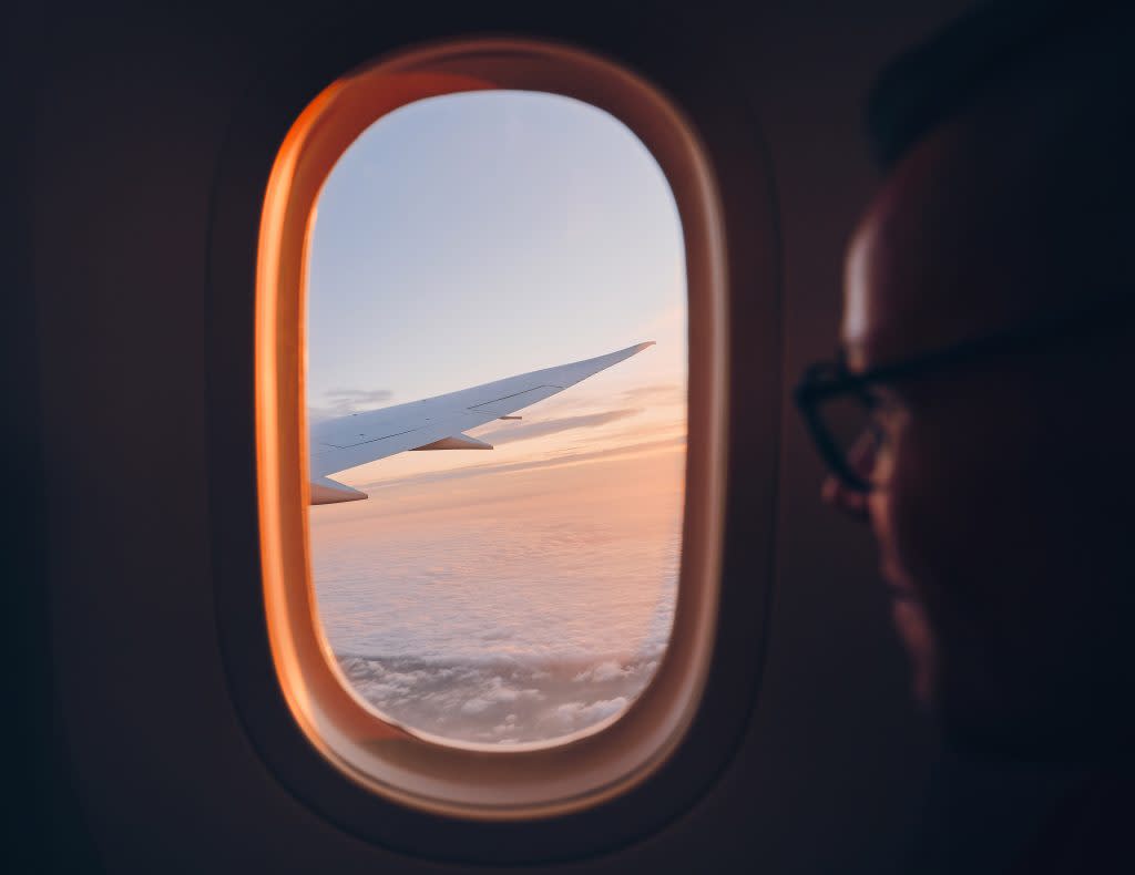 A man looks at the wing of an airplane from his seat on the airplane. 