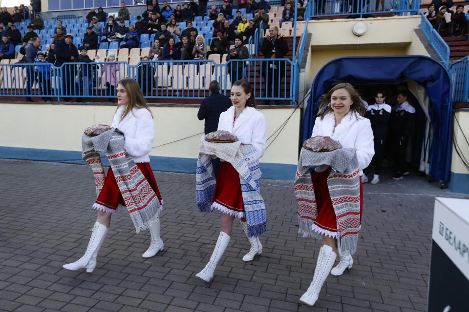 In this photo taken on Friday, March 27, 2020, women dressed in Belarusian national clothes carry traditional bread to greet players prior to the Belarus Championship soccer match between Torpedo-BelAZ Zhodino and Belshina Bobruisk in the town of Zhodino, Belarus. Longtime Belarus President Alexander Lukashenko is proudly keeping soccer and hockey arenas open even though most sports around the world have shut down because of the coronavirus pandemic. The new coronavirus causes mild or moderate symptoms for most people, but for some, especially older adults and people with existing health problems, it can cause more severe illness or death. (AP Photo/Sergei Grits)