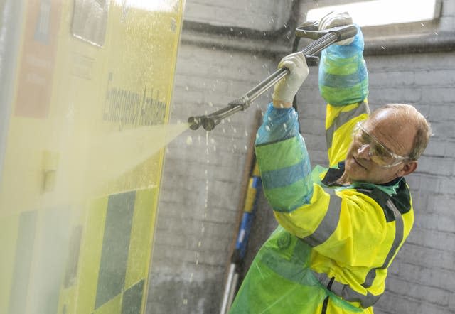 Sir Ed Davey wearing hi-vis uses a power hose to clean a bright yellow ambulance.