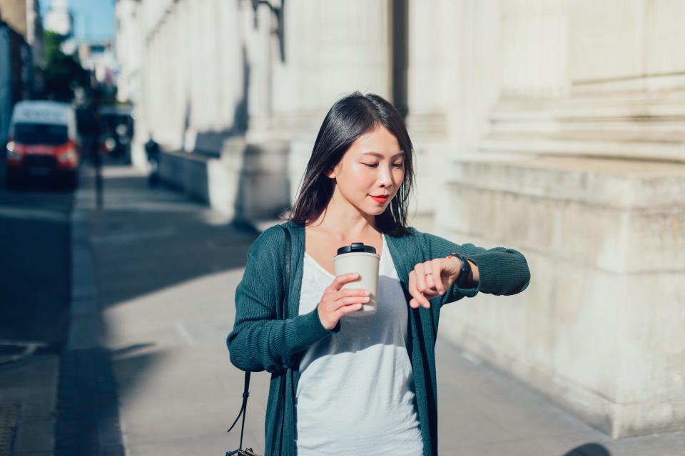 Woman Checking Time On Her Watch While Commuting To Work With Coffee