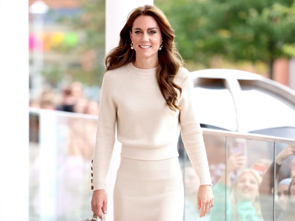 Kate Middleton walks in a cream sweater and coordinating skirt.