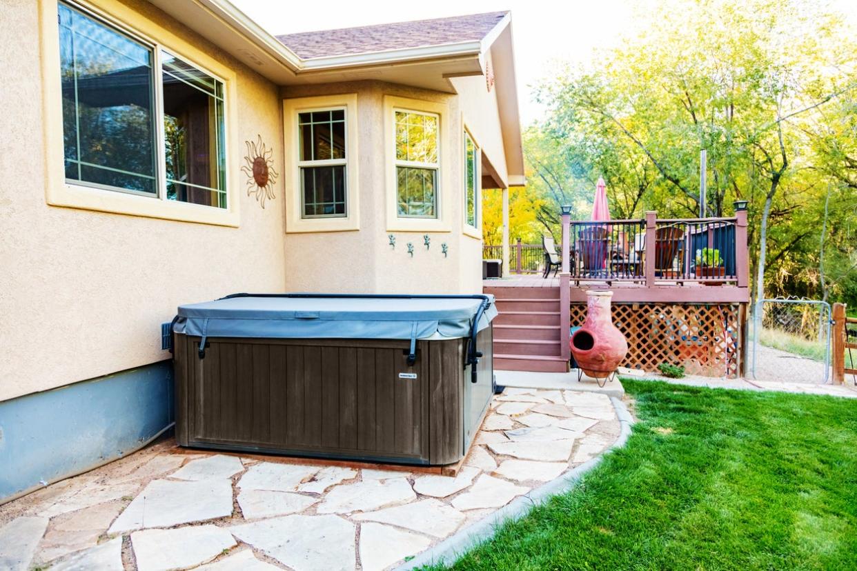 Home with aging hot tub on stone back patio.