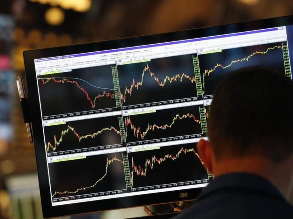 A screen displays stock charts while a trader works at his post on the floor at the New York Stock Exchange