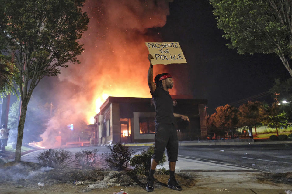 A person holds a sign as a Wendy's restaurant burns Saturday, June 13, 2020, in Atlanta after demonstrators allegedly set it on fire. Demonstrators were protesting the death of Rayshard Brooks, a black man who was shot and killed by Atlanta police Friday evening following a struggle in the Wendy's drive-thru line. (Ben GrayAtlanta Journal-Constitution via AP)