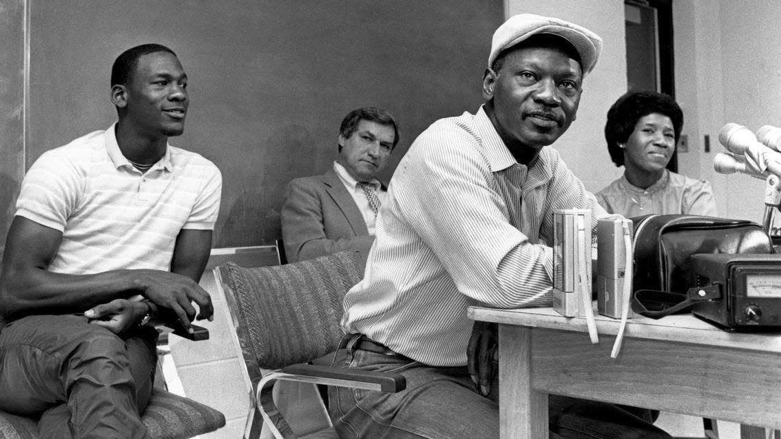 Michael Jordan (left) watches as his father James Jordan speaks with reporters at a press conference where he announced that he would leave the University of North Carolina early to enter the NBA draft. Jordan’s mother Deloris is at right and coach Dean Smith is at center rear.