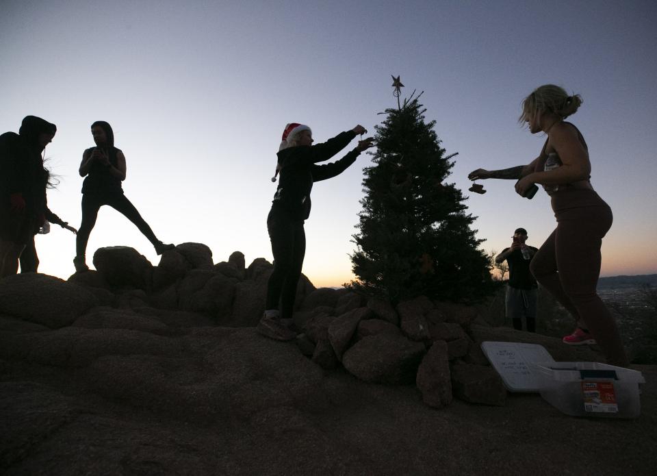 Kristi O’Hara (right) from Chandler and Jes Shapiro (center) from Phoenix, place bird seed ornaments on a Christmas tree on the summit of Camelback Mountain in Phoenix, just before  sunrise on Dec. 9, 2020.