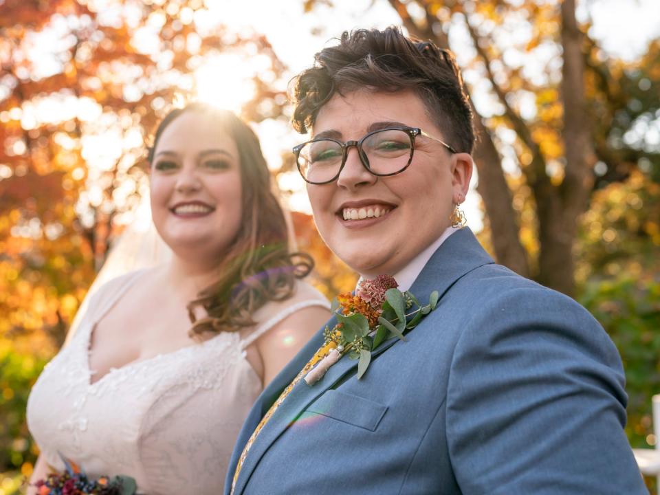 A couple grins on their wedding day in front of trees.