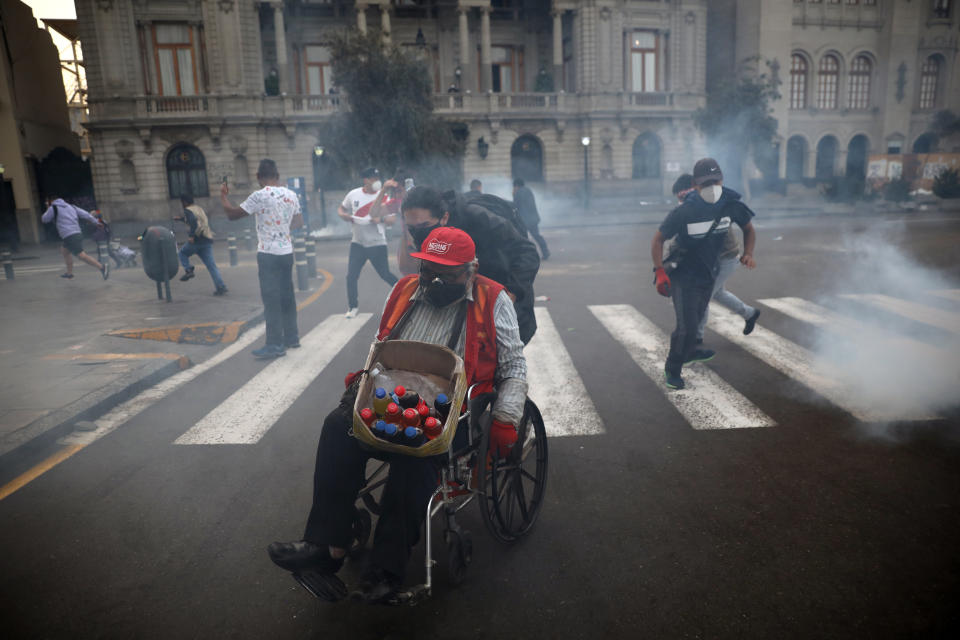 A protester helps a vendor in a wheelchair seek refuge from tear gas launched by police to disperse protesters near Congress where lawmakers swore-in a new president after voting to oust President Martin Vizcarra the day before, in Lima, Peru, Tuesday, Nov. 10, 2020. Peru swore in businessman and head of Congress Manuel Merino Tuesday who is unknown to most and was recently accused of trying to secure the military’s support for a congressional effort to boot the nation’s last leader out over unproven corruption allegations. (AP Photo/Rodrigo Abd)