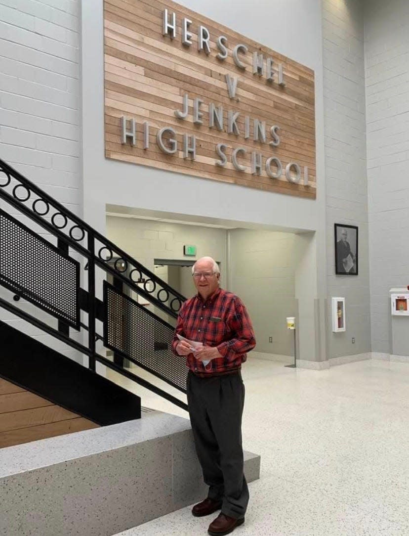 Don Stewart in front of the sign made from planed oak trees that stood in front of the original school.
