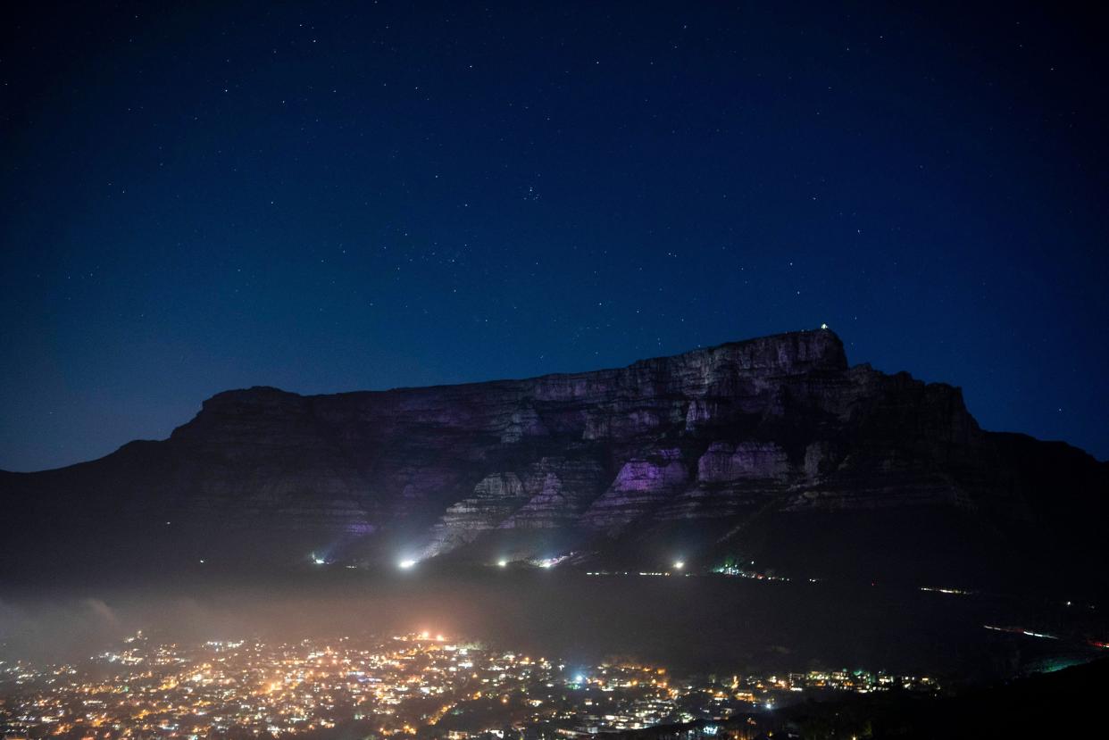This photograph taken on December 26, 2021 shows Table Mountain lit up with a faint purple glow to honour the memory of Archbishop Desmond Tutu, Nobel Peace Laureate, in Cape Town. - South African anti-apartheid icon Desmond Tutu, described as the country's moral compass, died on December 26, 2021, aged 90, President Cyril Ramaphosa said.