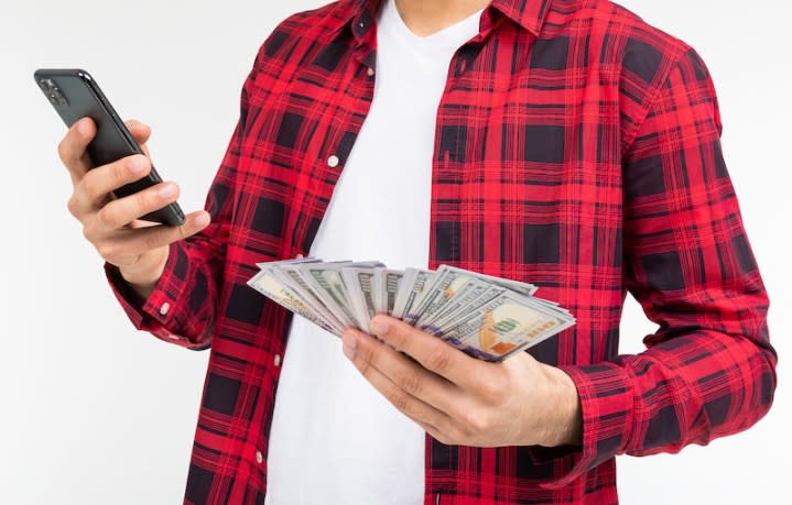 portrait of a cute guy with a bunch of money talking on the phone on a white studio background with copy space