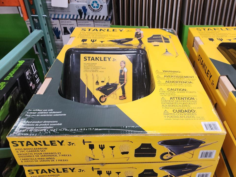 Yellow boxes of Stanley Jr/ wheelbarrows with an image of a young girl holding a wheelbarrow by the habndles