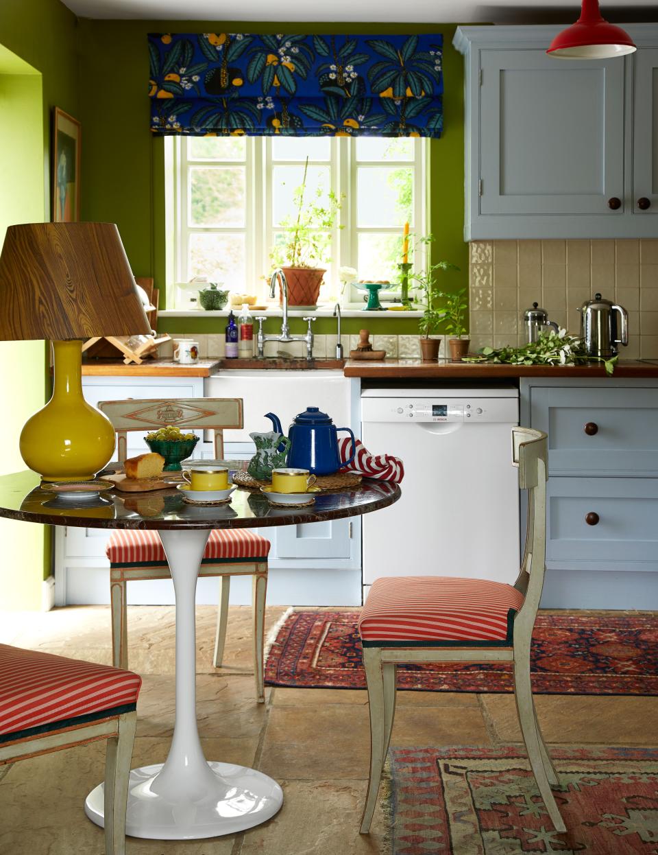 A Josef Frank cotton from Svenskt Tenn crowns a kitchen window; cabinets painted in a blue by Little Greene.