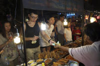 In this March 30, 2014 photo, Chinese tourists buy snacks while touring night market in Chiang Mai province, northern Thailand. The bucolic, once laid-back, campus of one of Thailand’s top universities seems to be under a security clampdown these days. Not against a terrorist threat, but Chinese tourists, thousands of them, who have clambered aboard student buses, eaten in cafeterias, sneaked into classes to attend lectures and even pitched a tent by a picturesque lake. Now visitors are restricted to entering through a single gate manned by Mandarin-speaking volunteers who direct Chinese tourists to a line of vehicles for guided tours. (AP Photo/Apichart Weerawong)