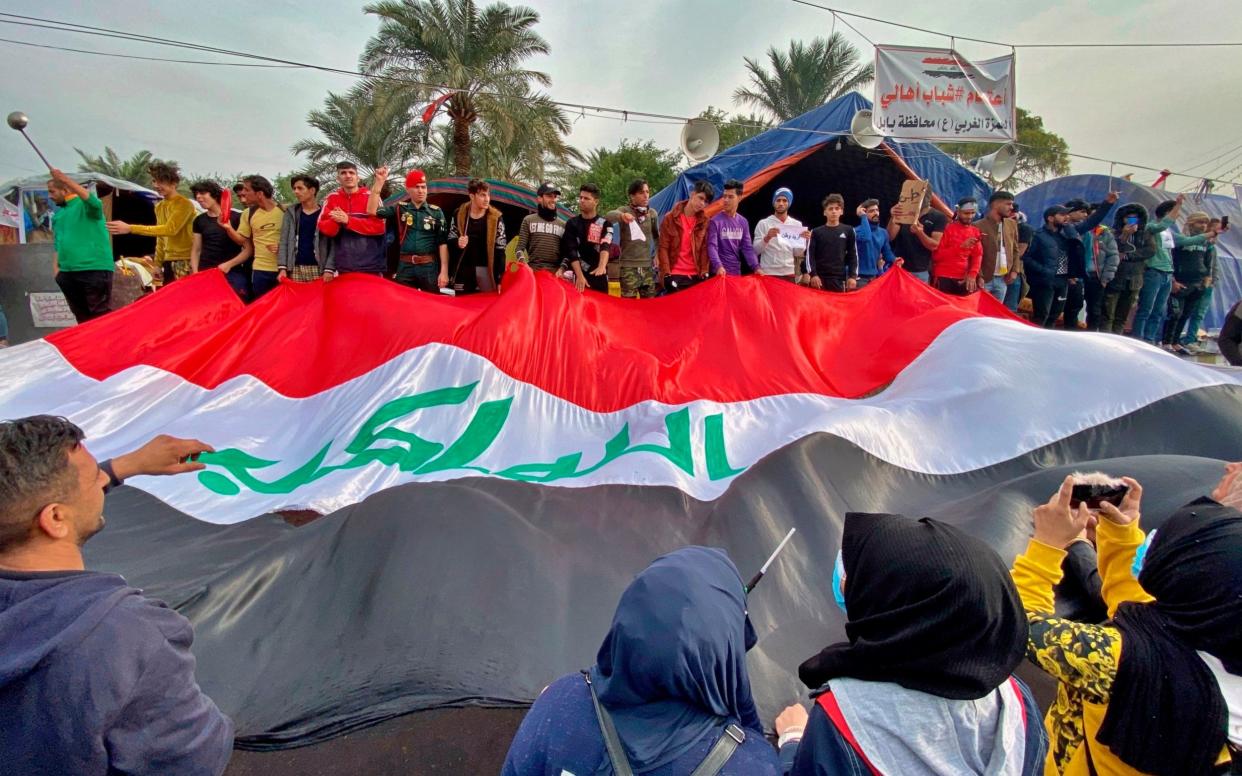 Anti-government protesters in Tahrir Square, Baghdad, hold a huge Iraqi flag after the lynching incident nearby was condemned by the wider protest movement - AP