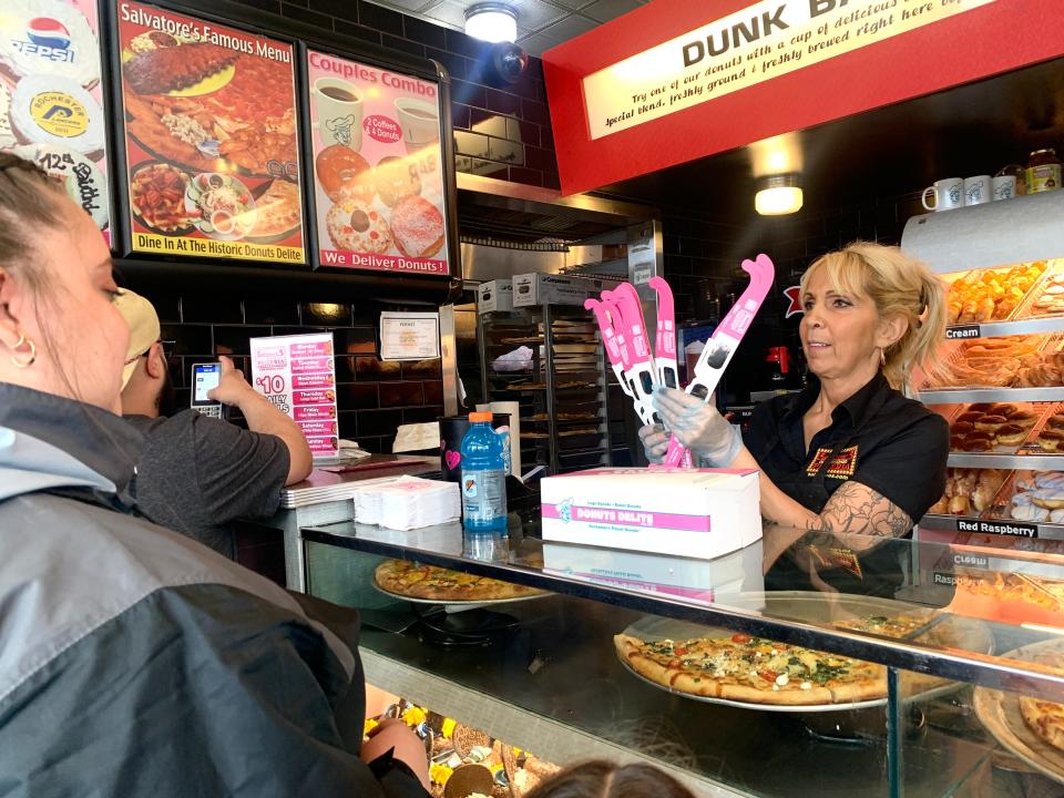 Deanna DeNoto of Donuts Delite hands out branded eclipse glasses to Brianna Casanova at Donuts Delite on April 8, 2024.