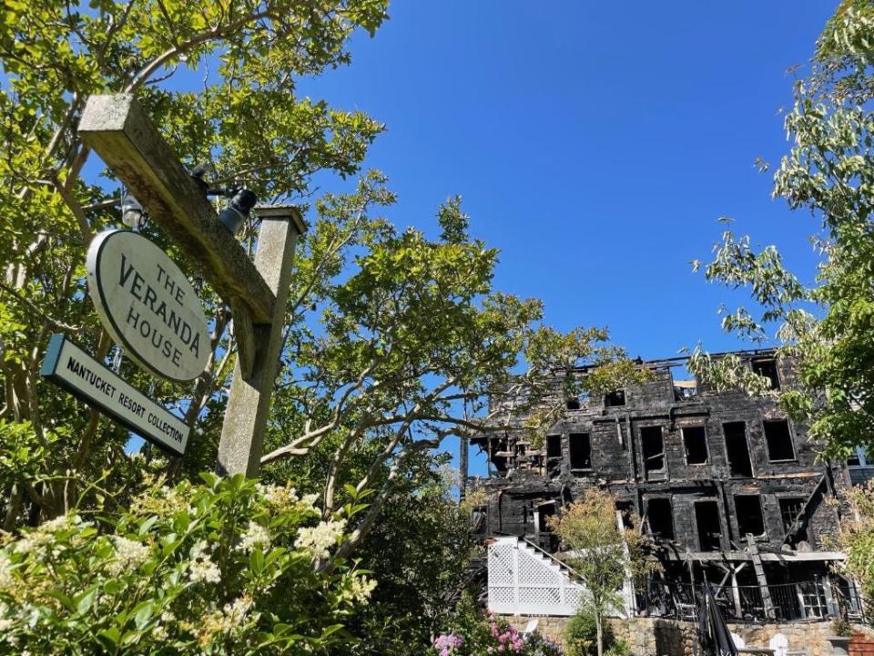 The charred remains of the Veranda House on Nantucket are a backdrop to the inn's sign after a morning fire Saturday.