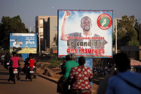 People ride motorcycles past a billboard for presidential candidate Benewende Sankara in Ouagadougou, Burkina Faso, November 28, 2015, ahead of the election. The billboard reads, "Vote Benewende Sankara, the insurgents' candidate." REUTERS/Joe Penney