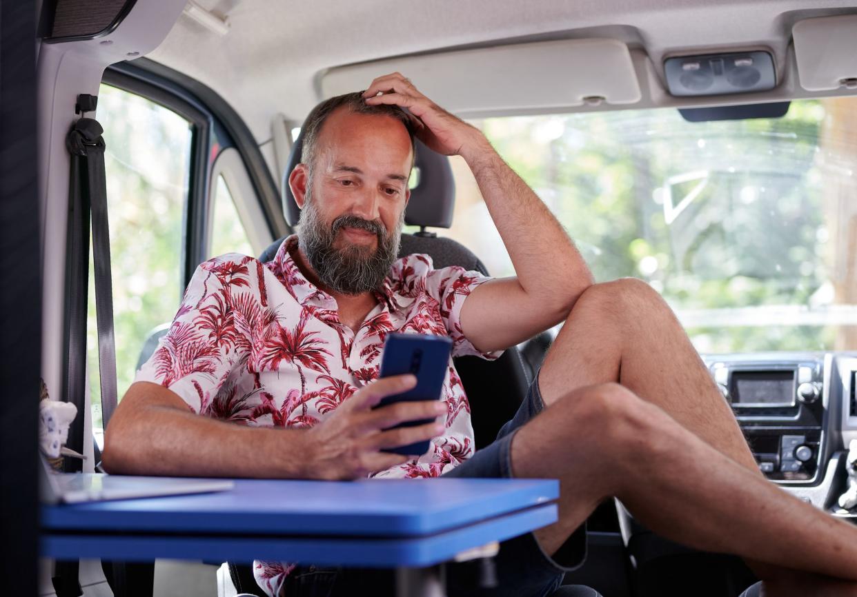 middle-aged bearded man in summer shirt smilingly looking at his mobile phone inside his motor home