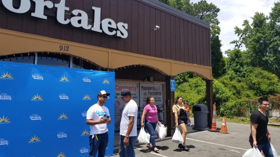 While shoppers exit the  Los Portales store with grocery bags, Douglas Barbera, a volunteer with the LIBRE Initiative, far left, speaks to a customer about inflation, while passing out gift cards for the store.