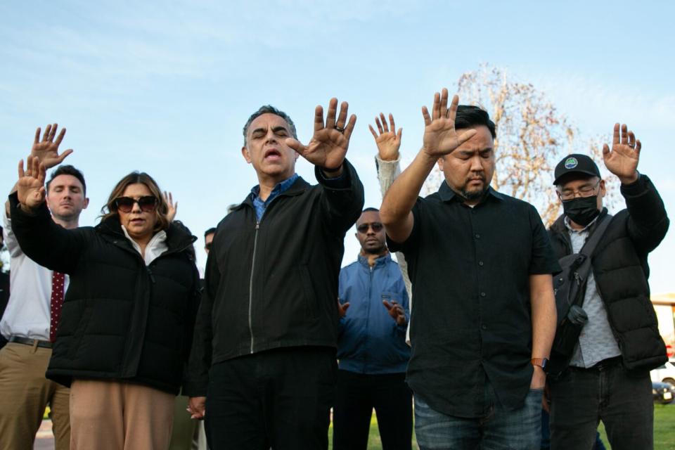 Faith leaders and community members hold up their hands while standing together.