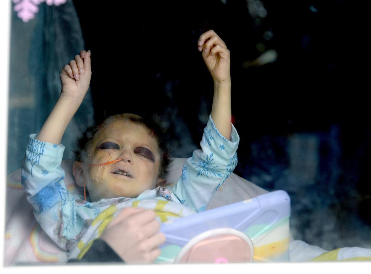 June Peden-Stade, 3, of Auburn, who has cancer, reacts as she watches through her screen door window as the Make-a-Wish parade for her passes by her home Saturday.