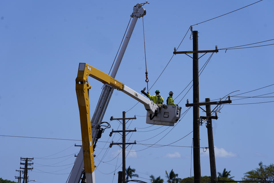 FILE - Linemen work on poles, Sunday, Aug. 13, 2023, in Lahaina, Hawaii, following a deadly wildfire that caused heavy damage days earlier. Hawaiian Electric Co. faces criticism for not shutting off the power amid high wind warnings and keeping it on even as dozens of poles began to topple. (AP Photo/Rick Bowmer, File)